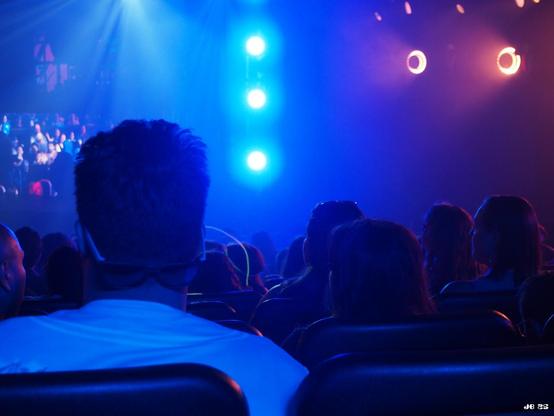 Innenaufnahme bei einem Auftritt der Blue Man Group in Las Vegas von den Zuschauerrängen in Richtung Bühne. Alles ist in blaues Licht getaucht. Fünf runde Lichter - drei übereinander in Bildmitte und zwei weiter oben rechts - stechen heraus.