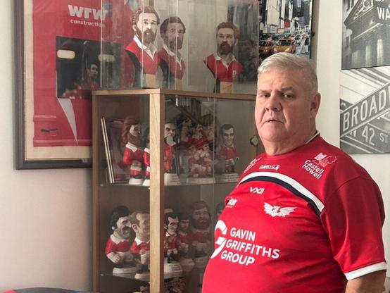 Llanelli mayor Andrew Bragoli stands in a Scarlets shirt in front of his memorabilia collection, showing his support for the Save Our Scarlets campaign.