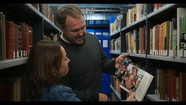 Scott Quinnell and presenter Dot Davies examine a book in the Reading Room of the National Library of Wales during filming of Cyfrinachau’r Llyfrgell.