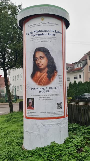 Litfassäule mit die ganze Höhe füllendem Plakat, das einen Vortrag eines Schülers des Yoga-Lehrers Yogananda ankündigt. Dessen porträt mit langem Haar und verklärtem lächeln bewusst riesengross.