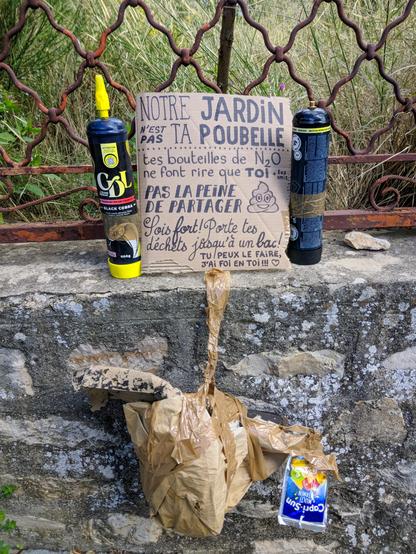 Photo d'une pancarte en carton posée sur un muret de jardin, à laquelle sont scotchées des ordures (sac de repas, pochon Capri-Sun, bouteilles de protoxyde d'azote). Un message sur le carton dit : "Notre jardin n'est pas ta poubelle ! Tes bouteilles de N2O ne font rire que toi. Pas la peine de partager. Sois fort ! Porte tes déchets jusqu'à un bac ! Tu peux le faire, j'ai foi en toi."