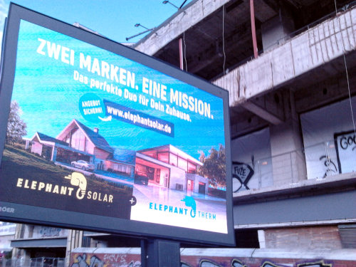 Ströer-Displaywerbetafel vor der zerfallenden Fassade der Ruine des Ihmezentrums in der Spinnereistraße in Hannover-Linden. Angezeigte Werbung »Zwei Marken. Eine Mission. Das perfekte Duo für Dein Zuhause. www.elephantsolar.de. Elephant Solar + Elephant Therm«.