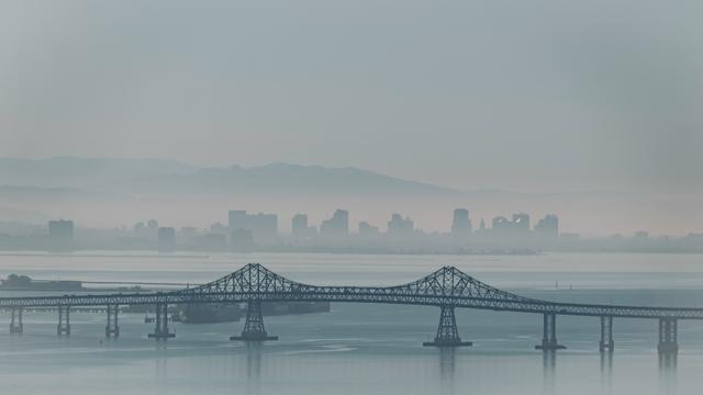 A view over water on a hazy morning. The buildings of Oakland standing out against the haze behind - seen over the Richmond Bridge from the China Camp Trails, San Rafael, Marin.  The tankers coming in/out of the Richmond refineries seen just beyond the bridge on the left.  San Francisco would be off to the right, out of frame.