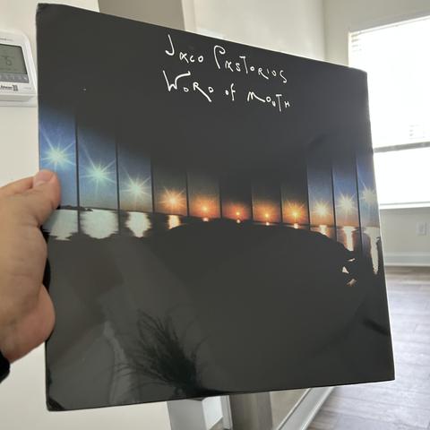 A photo of my left hand holding Jaco Pastorius’ Word of Mouth vinyl LP.