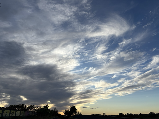 A blue evening sky with curly-wurly clouds in grey and white, highlighted by the sun