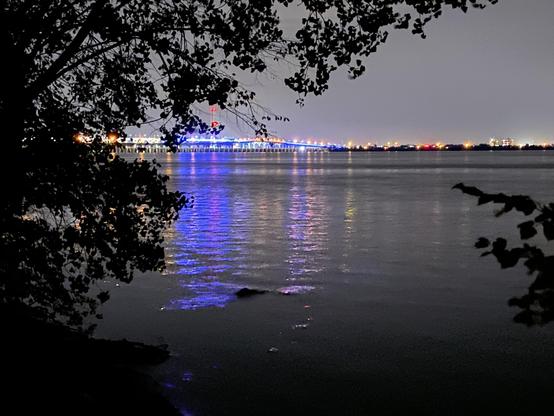 Photo of the Samuel-de Champlain Bridge from about 3km away at night.

It is illuminated in neon blue. On the right, we can see the odd lights from the city of Brossard.

In the foreground, the calm Saint-Lawrence River and a few tree branches. 
- - -
Photo du pont Samuel-de-Champlain à environ 3 km de distance la nuit.

Il est éclairé en bleu néon. Sur la droite, nous pouvons voir les quelques lumières de la ville de Brossard.

Au premier plan, le fleuve Saint-Laurent calme et quelques branches d'arbres.