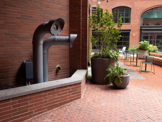 A side view shows the artwork's proximity to a central square within its host development.