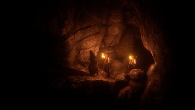 A dimly lit cave scene featuring two men seated around a central campfire, engaged in conversation. The man on the left is holding a lit torch, casting a warm glow across his face and attire. The other man sits facing him, with an alert posture. Rocky walls form the backdrop of this intimate setting.