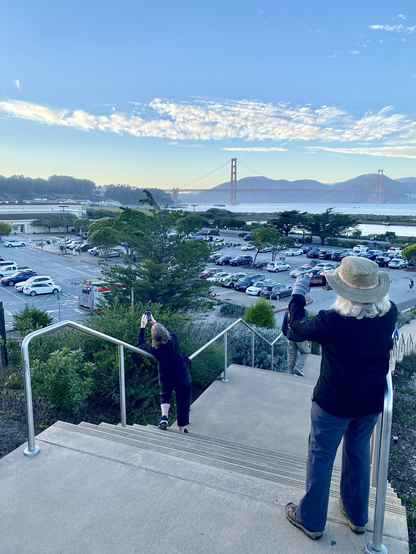 From the top of a grand stairway at Tunnel Tops, people are taking photos of the Bay and the Golden Gate Bridge