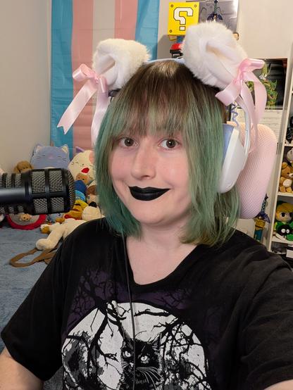 Revy smiling and wearing black lipstick 
She has cat ear headphones on and is next to a microphone