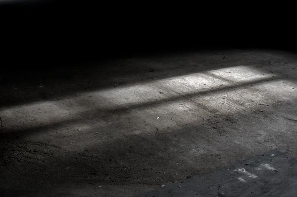 Auf nacktem Betonboden wird ein Schatten eines Fensters mit Querstreben geworfen