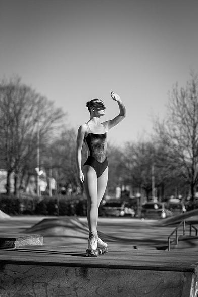 Rollkunstläuferin in ihrem Sportoutfit auf der Halfpipe eines Skateparks im hellen Sonnenlicht stehend und die linke Hand ausgestreckt, um sich das Gesicht abzuschatten.