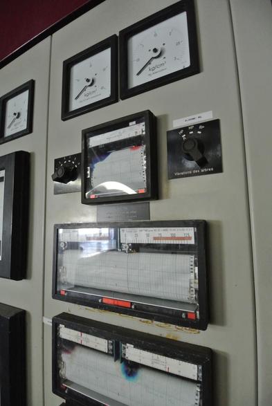 Drei Seismographen an einer Kontrollwand. Daneben Knöpfe und anzeigeuhren