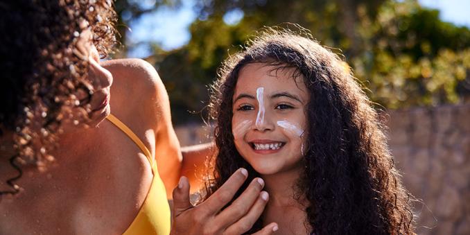 Woman applying sunscreen to a young child outdoors, highlighting the importance of sun safety and skin cancer prevention.