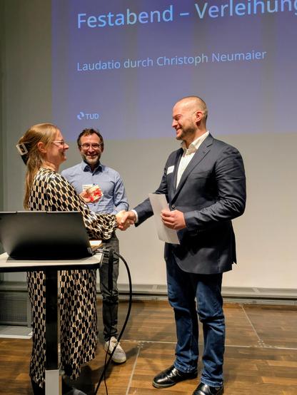 Nadine Metzger and Christopher Neumaier hand over the document to Achim Klüppelberg on a stage at the German Hygiene Museum in Dresden.