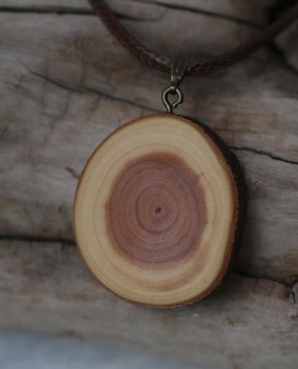 A yew pendant sanded all shiny, on a faux leather chain, resting on a piece of driftwood.