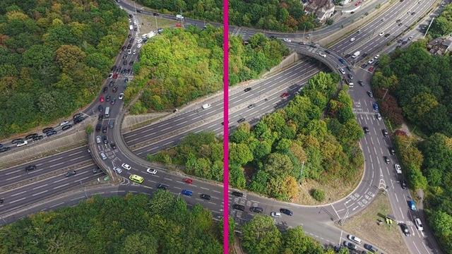 Aerial view of a multi-lane highway interchange with curved roadways and connecting ramps, surrounded by dense green vegetation and trees, with a bright pink vertical line dividing the image down the center and vehicles visible traveling in multiple lanes.