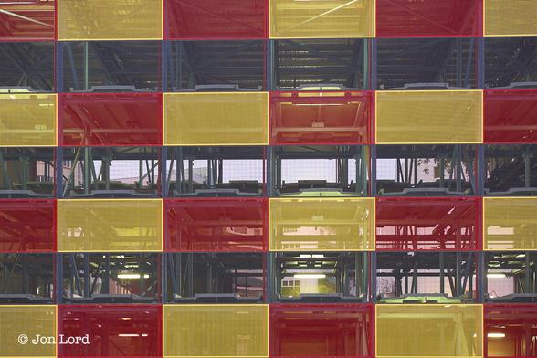 This is a colour abstract photo of the facade of a multi-story car park.
The entire frame is filled with a coloured checkerboard pattern of rectangular yellow, red and transparent surfaces. The coloured rectangles are arranged horizontally in alternating strips: red, yellow, red and so on. Vertically are alternating transparent strips, which in fact empty allowing one to see through the structure. So vertically it's one coloured strip, transparent strip, coloured strip etc. The coloured strips are made of a fine mesh and themselves very slightly  transparent. The clear strips are also made from a fine mesh but are almost totally transparent. Within the structure is a lattice metal framework.
As I remember this was a small multi-story automated car park, though there were no cars visible.
The Location: Outram, Singapore (2012).