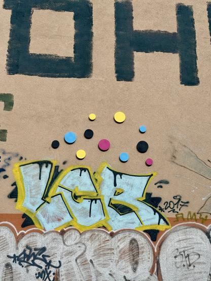 Wand mit Kreisen in Zyan, Magenta Gelb und Schwarz. Und diverse Graffiti.