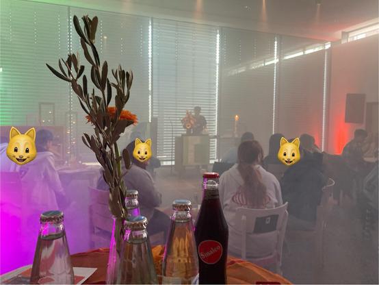 Ein moderner Gottesdienstraum mit Jugendlichen bei Licht und Nebel. Ein Tisch mit Blume und Softdrinks im Vordergrund.