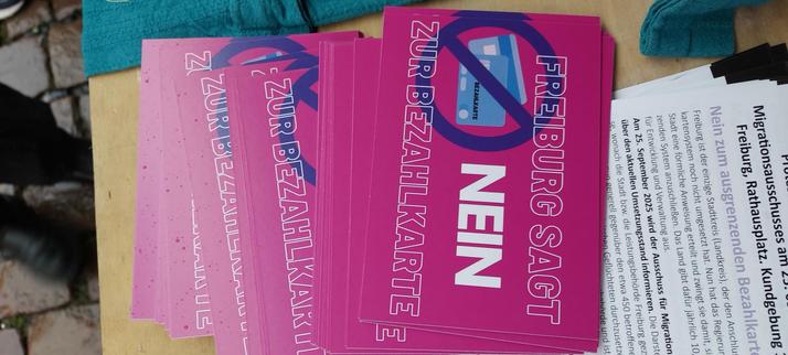 Pinke Flyer auf einem Tisch mit der Aufschrift "Freiburg sagt NEIN zur Bezahlkarte".