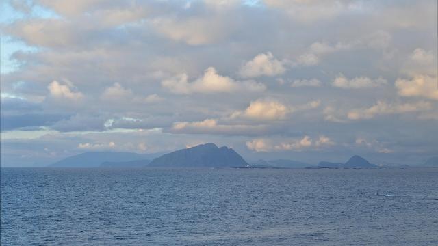 A photo of the Norwegian Sea with mountains in the distance. The sky is filled with clouds.