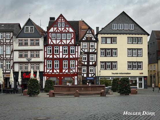Weitwinkelaufnahme des Butzbacher Marktplatzes mit Brunnen in der Mitte, umgeben von Fachwerkhäusern.
