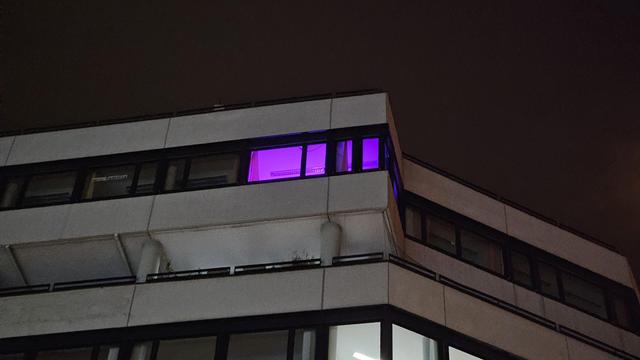 Der obere Teil eines Bürogebäudes. Im Hintergrund der dunkle Himmel.
Ein Büro ist lila erleuchtet.