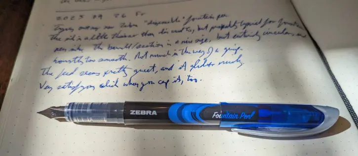 A posted blue Zebra fountain pen on top of a journal page which reads:

2025 09 26 Fr
Trying out my new Zebra "disposable" fountain pen.
The ink is a little thinner than I'm used to, but probably typical for fountain pen inks. The barrel/section is a nice size, but entirely circular, and honestly too smooth. Not much in the way of a grip. 
The feed seems pretty great, and it glides nicely. 
Very satisfying click when you cap it, too.