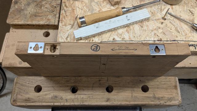 Larger view, the two metal plates sit in a mortise on the backside of a small shelf board. One plate is not yet screwed in, and the mortise behind it can be seen where the head of the screw in the wall will come to rest.