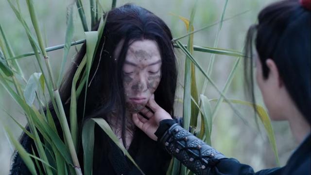 Wei Wuxian is partially visible at the right side of the image, right arm outstretched as he lightly holds Wen Ning's chin. Wen Ning stands with eyes downcast, mud smeared across his face and neck, and tall stalks of green plants strapped to his body.