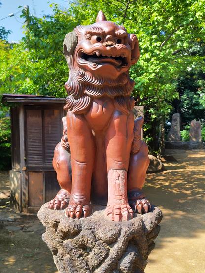 It's a half dog half something undefined version of a guard animal. There are typically are couple of them, one on either side of the path leading to the shrine. We are looking at the one on the right hand side. It's sitting on a stone pedestal at about hip height and is about 75cm or 2.5ft tall. It's made from a cast in bronze. It's left leg must have been damaged and has been replaced by wood carved in the right shape.