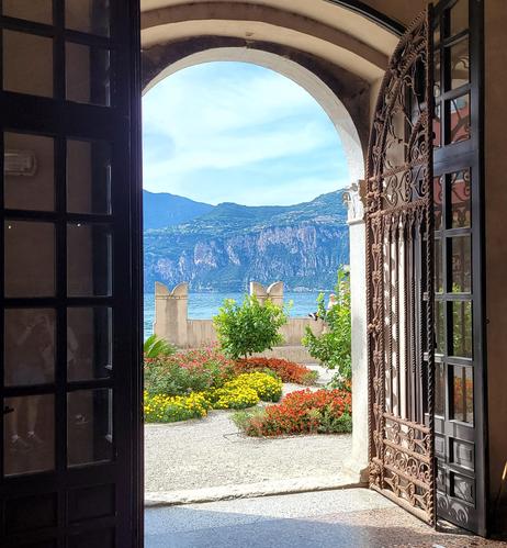 Blick durch ein kunstvollesTor eines Innenhofes auf mediterranen Garten und See