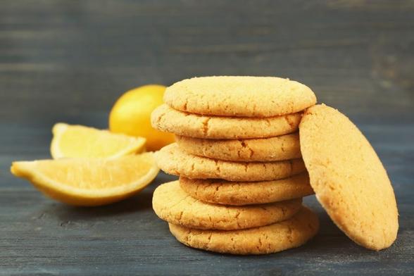 Galletas caseras de masa sobada con limón apiladas sobre una superficie de madera oscura, con cuartos de limón al fondo.
