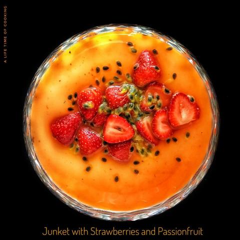 A vibrant dessert of yellow junket, red strawberries, black passionfruit seeds and the golden-pink-red juice of the macerated fruit.