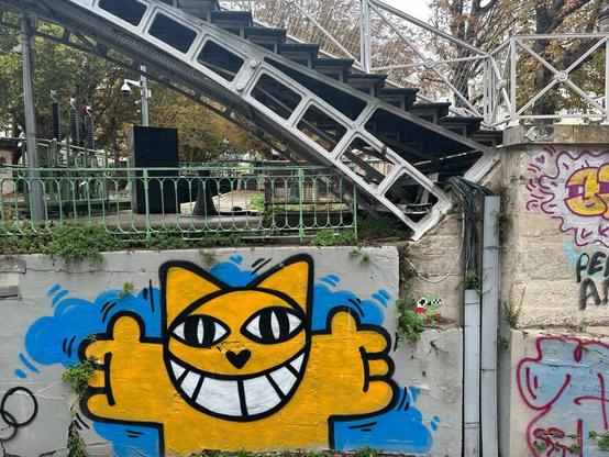 an aerosol-art piece of a cartoon cat anthropomorphically extending its arms as if offering a hug, on the side of a concrete bridge