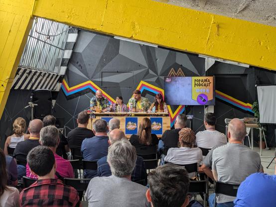 Los 4 protagonistas del podcast en una mesa ante el público en una sala de aspecto industrial