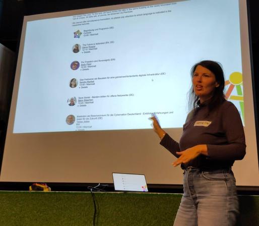 Samvie standing in front of a large screen with the avatars and handles of the speakers for #Fediday
