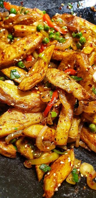 Chinese Salt & Pepper Chips, in the wok. Fresh oven baked chips, with onion, red pepper, peas, sesame seeds, spices, LOTS of chilli & salt & pepper.