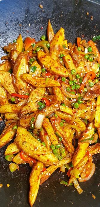 Chinese Salt & Pepper Chips, in the wok. Fresh oven baked chips, with onion, red pepper, peas, sesame seeds, spices, LOTS of chilli & salt & pepper.
