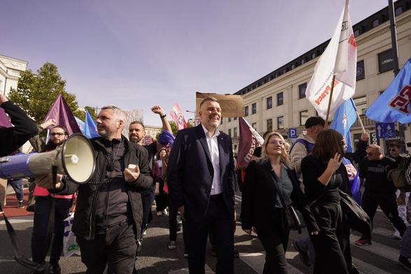 Maciej Konieczny, Adrian Zandberg i Aleksandra Owca maszerują na ulicy w tłumie ludzi. Widać flagi Razem i OPZZ.