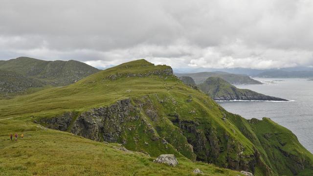 A photo of green hills with jagged coastlines. The sky is cloudy.