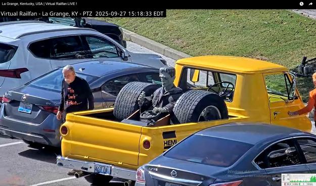 Ein alter gelber Minitruck mit einem nachgebautem Drag-Race-Fahrzeug auf der Ladefläche, in welchem eine Frankensteinfigur sitzt

Das Fahrzeug steht in La Grange - Kentucky - USA auf einer Straße mit einer Schiene, auf welcher sporadisch lange Güterzüge fahren.
Dort findet ab und zu ein Treffen aufgearbeiteter alter Fahrzeuge statt