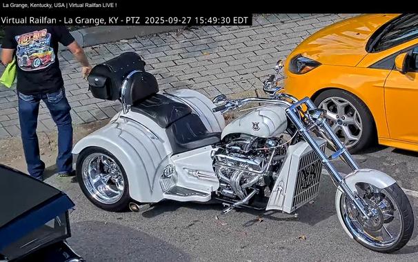 ein weißer Dreirad-Chopper mit breiten Hinterrädern, welche oben mit weißen Radblechen verkleidet sind und zur Seite chromglänzend sind
Die schwarze Sitzfläche ist mehrfach geteilt
Vor dem großen  chromglänzenden Motor ist ein weißer Wasserkühler angebaut

Das Fahrzeug steht in La Grange - Kentucky - USA auf einer Straße mit einer Schiene, auf welcher sporadisch lange Güterzüge fahren.
Dort findet ab und zu ein Treffen aufgearbeiteter alter Fahrzeuge statt