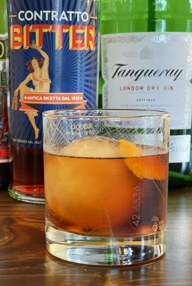 A cocktail in a rocks glass sits on a wooden surface in front of three liquor bottles.