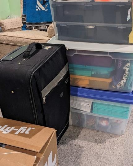 three bins of product stacked next to a suitcase and a repurposed polyfil box