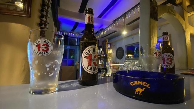 Tresen einer Kneipe. Auf diesem stehen zwei Bierflaschen, zwei Gläser und ein Aschenbecher. Es sind keine Menschen zu sehen.