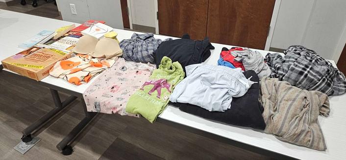 A photo of a white plastic table with folded clothing items laid out all over it and a few books and games.