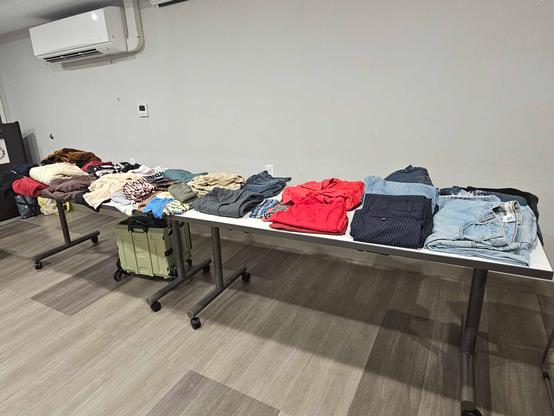 A photo of two more long white plastic tables covered with folded clothing.