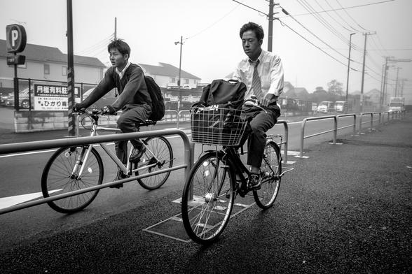 Dos homes muntats en bicicleta van cap a la feina en un dia boirós.